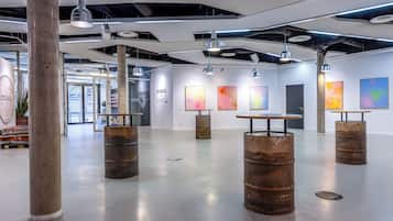 An art gallery with industrial-style lighting, concrete pillars, and abstract paintings on the walls.