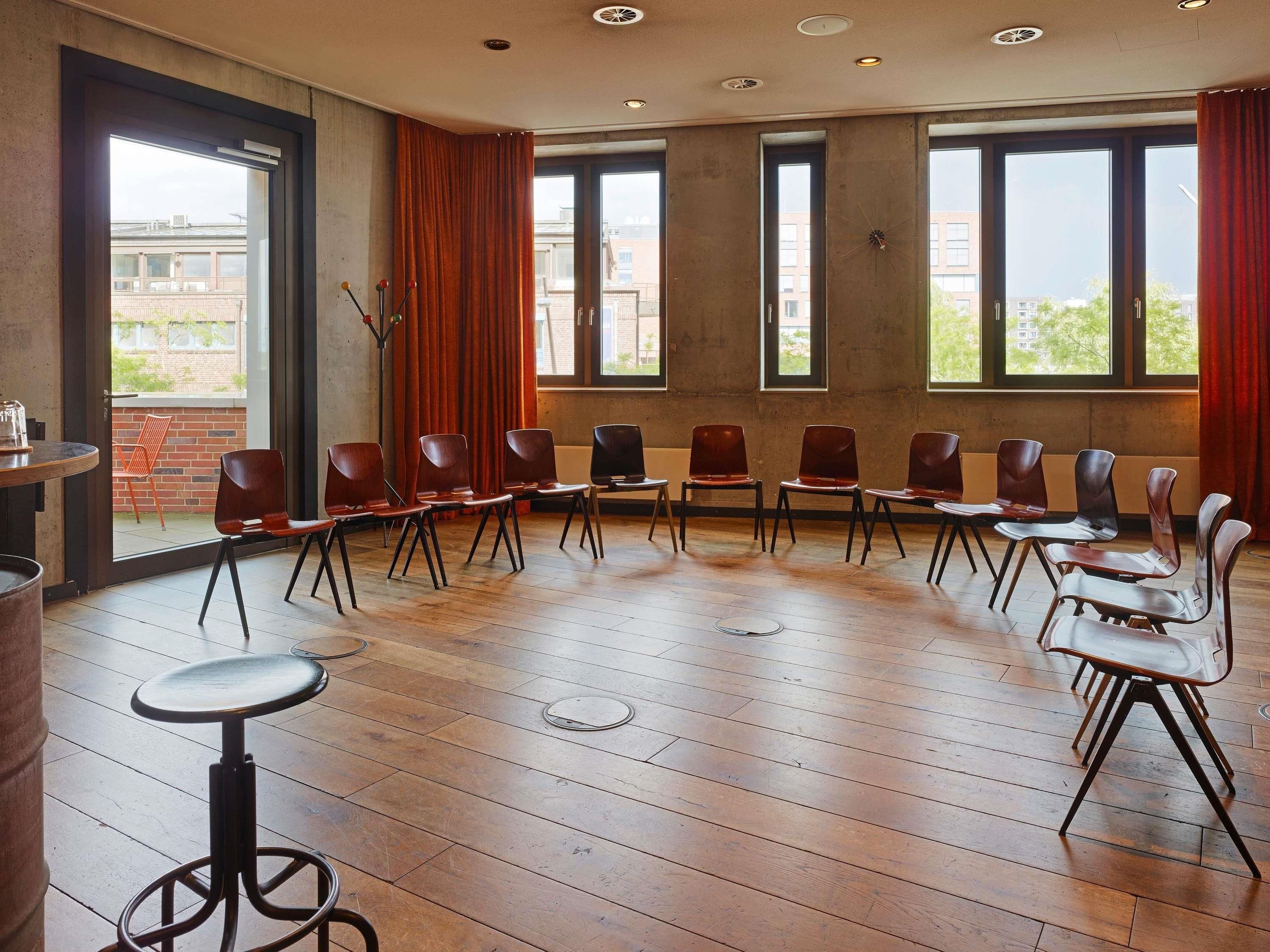 Een congreszaal met houten vloeren, een lange tafel en stoelen eromheen.