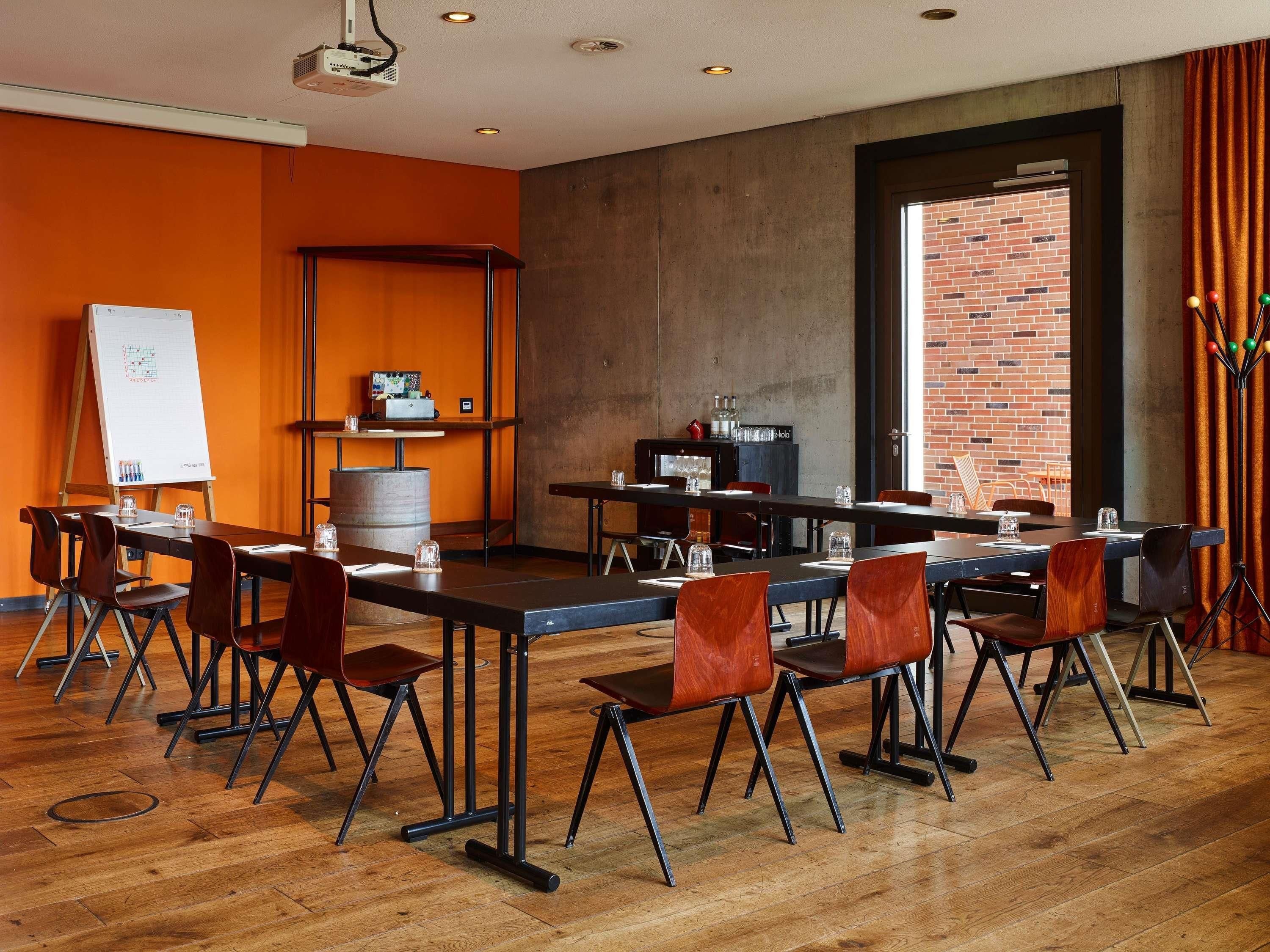 Uma sala de conferências com quadro branco, projetor e mesas com cadeiras.