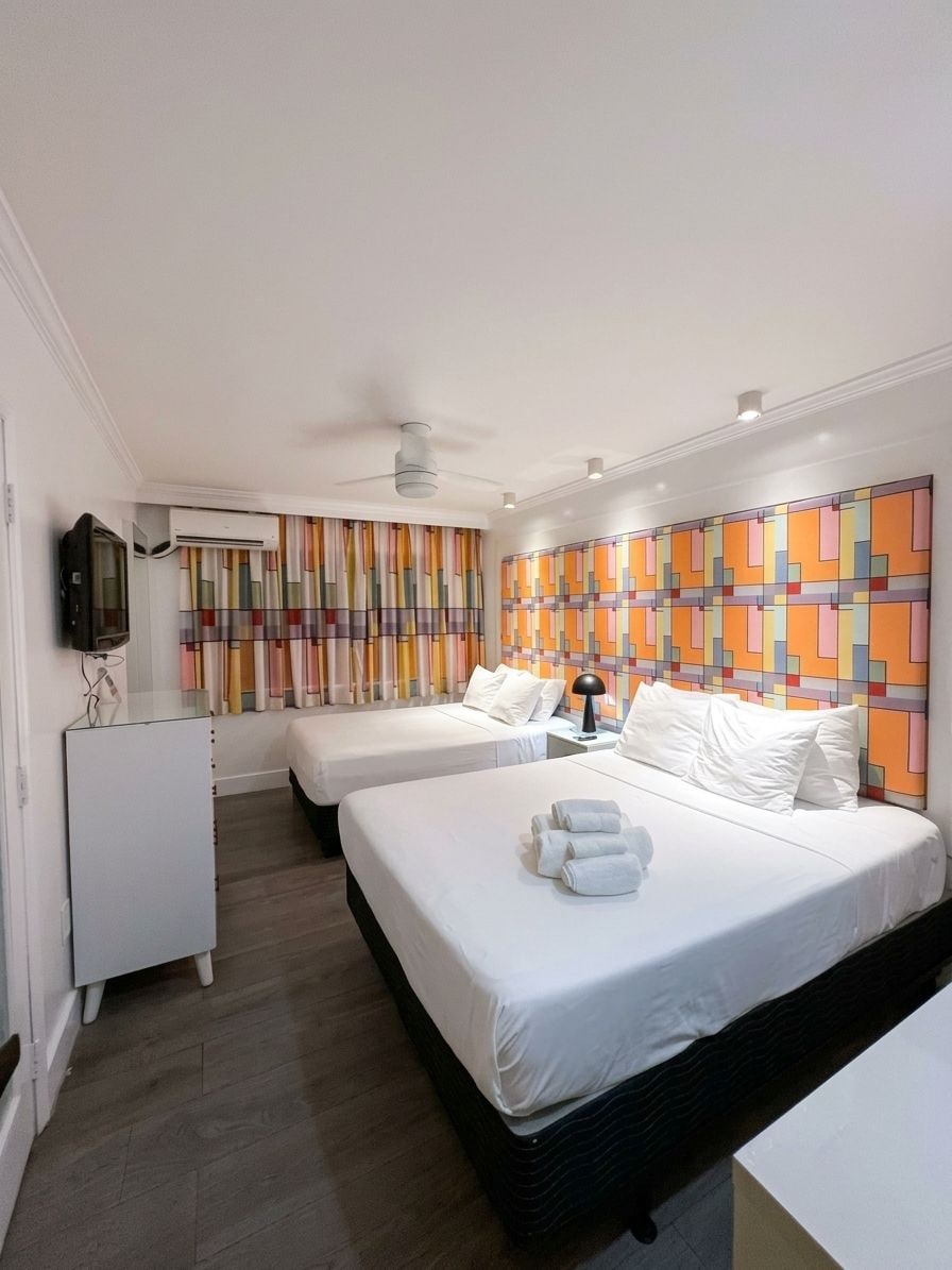 Habitació d'hotel amb dos llits, televisió, escriptori i un mur de colors.