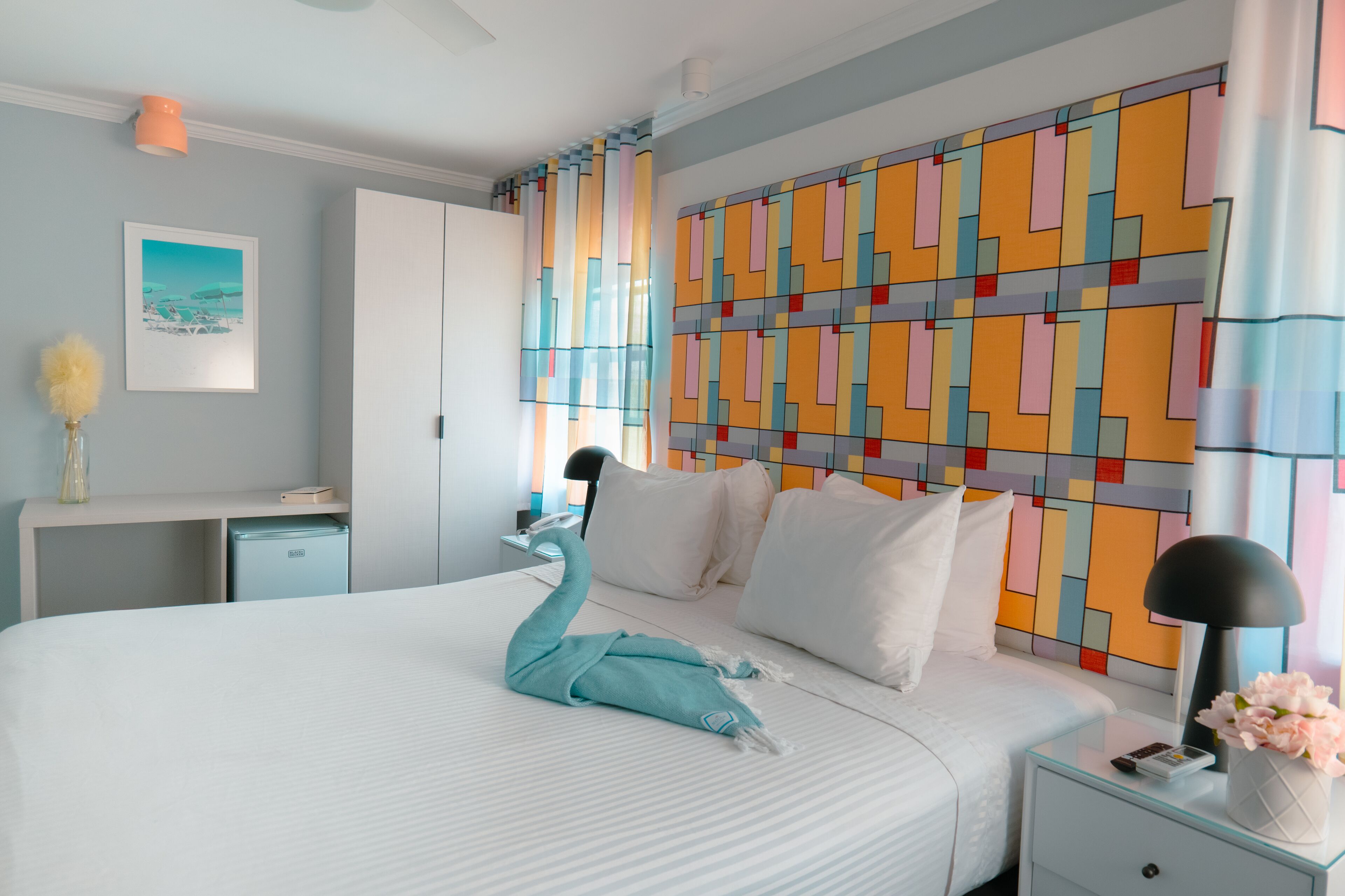A hotel room with a bed, a nightstand, a desk, a wardrobe, and a colorful wall.