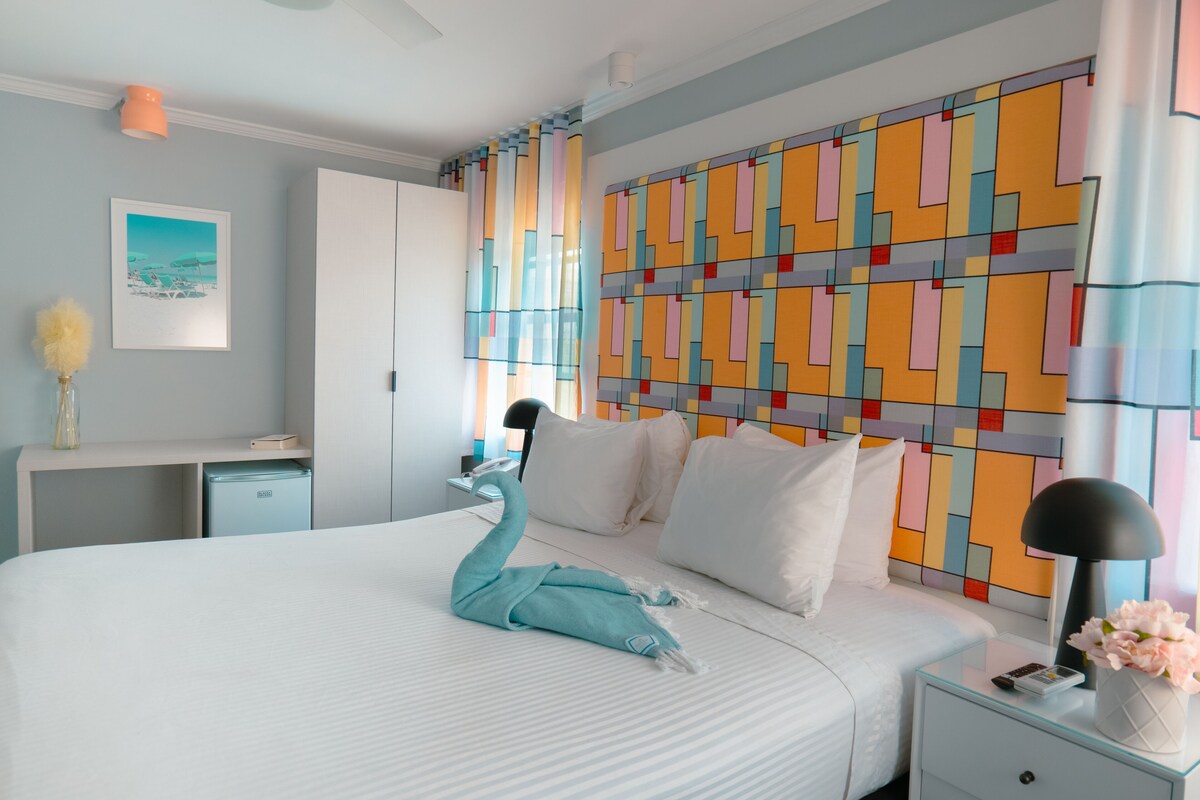 A hotel room with a bed, a nightstand, a desk, a wardrobe, and a colorful wall.