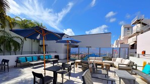 Eine Dachterrasse mit Sitzgelegenheiten im Freien, Sonnenschirmen und Blick auf die Stadt.