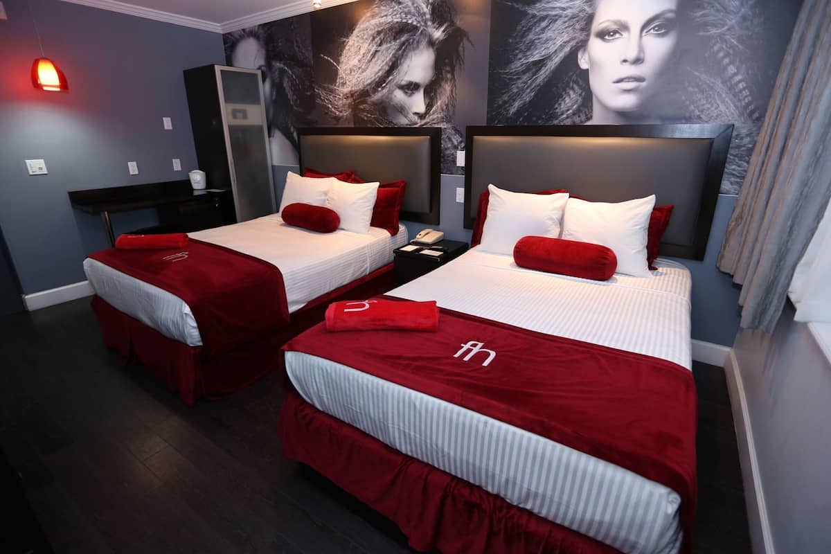 A hotel room with two beds, each with red and white bedding, a nightstand with a phone, and a wall-mounted mirror.