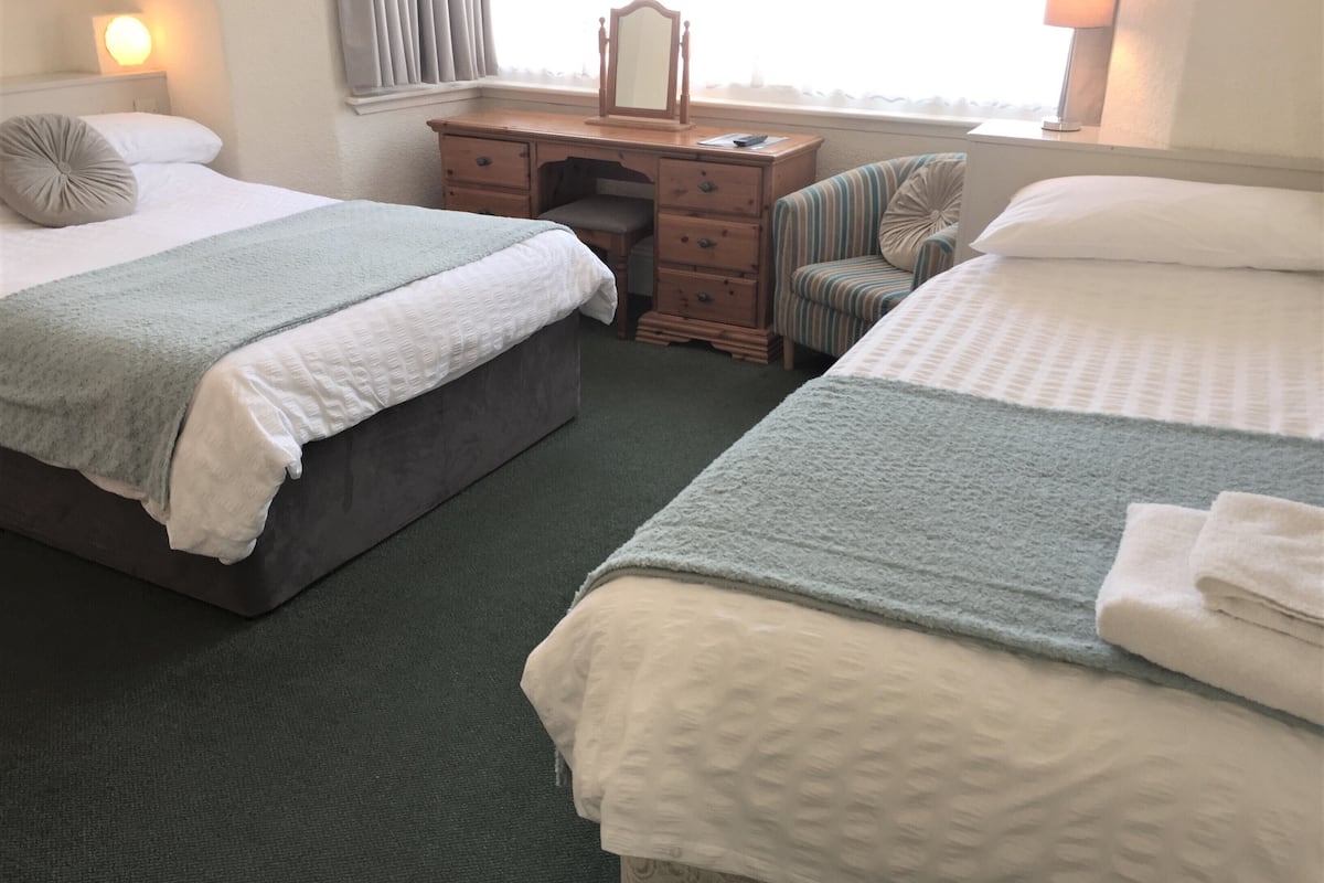 Una habitación de hotel con dos camas, un aparador, una silla y una ventana con cortinas.