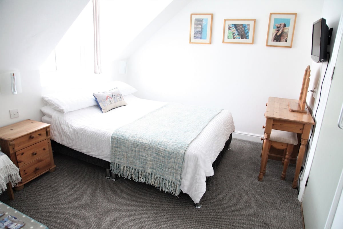 Un dormitorio con una cama, una mesita de noche de madera, un escritorio y una silla. Hay tres cuadros enmarcados en la pared.