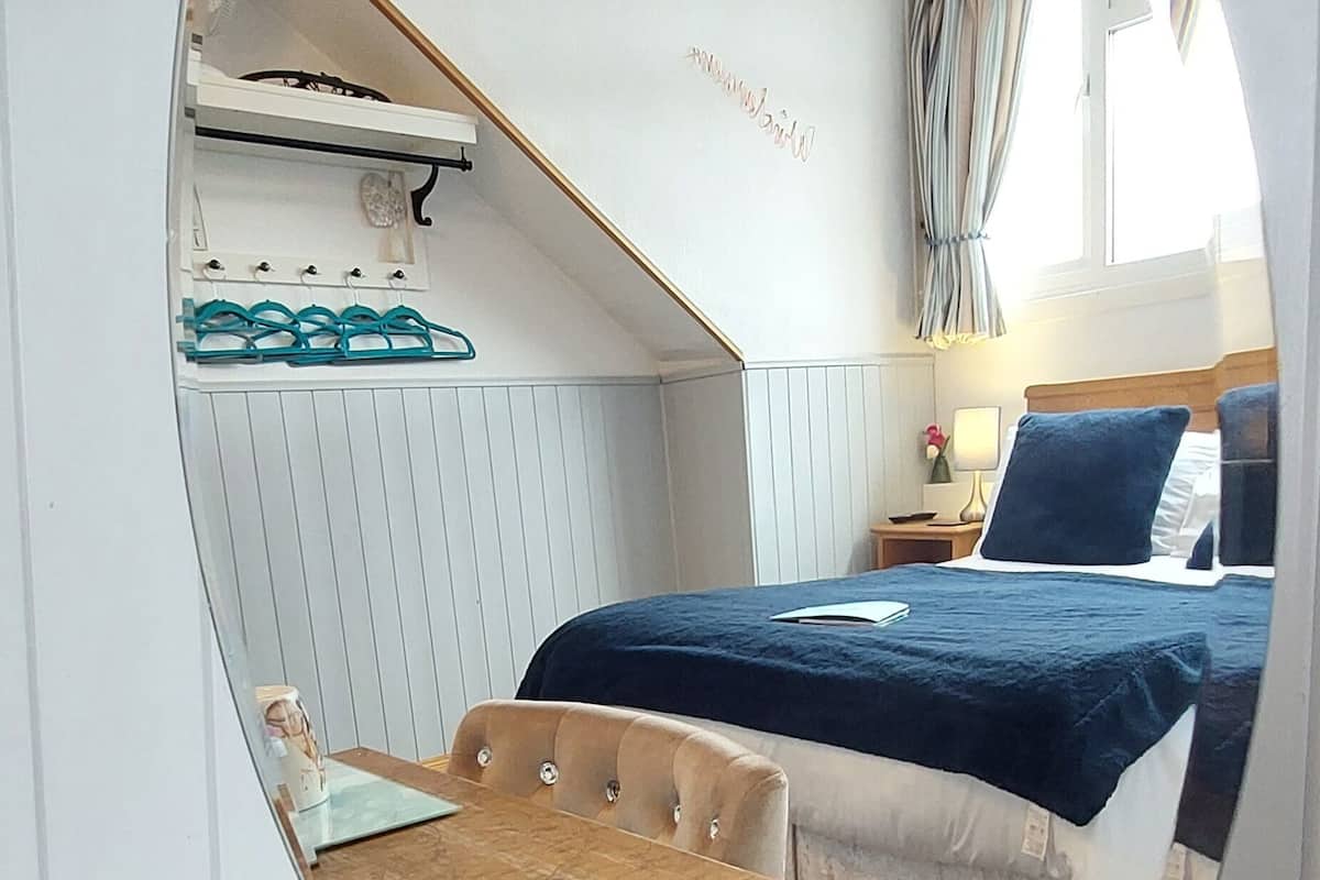 Ein Zimmer mit einem Bett, einem Nachttisch, einem Spiegel und einem Vorhangfenster.