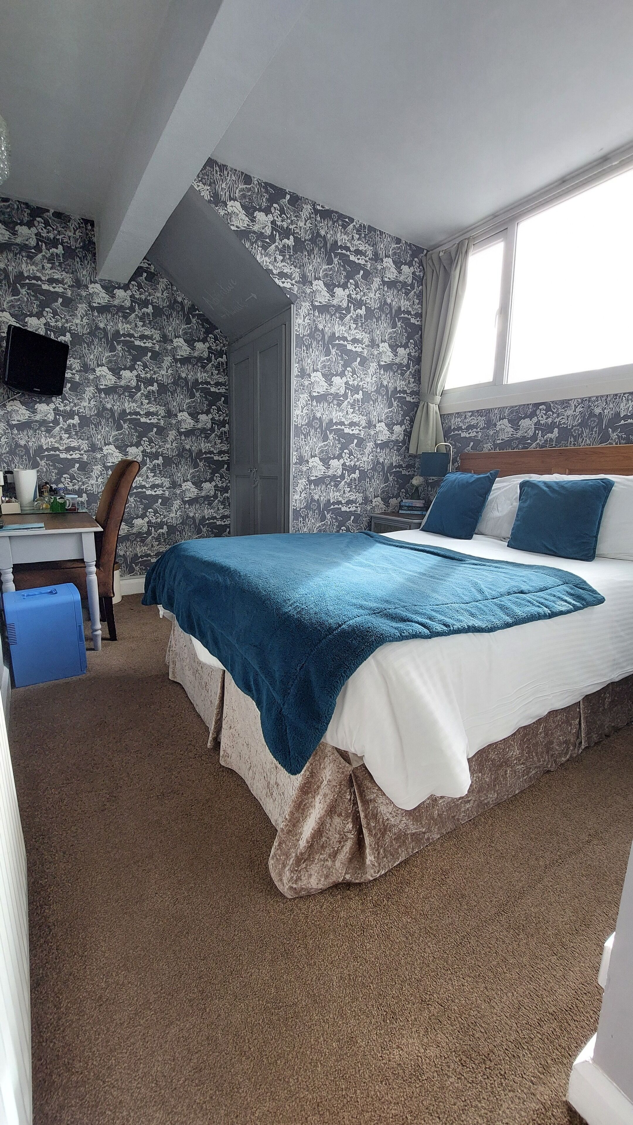 Un dormitorio con una cama, un escritorio, una silla y un televisor en la pared.