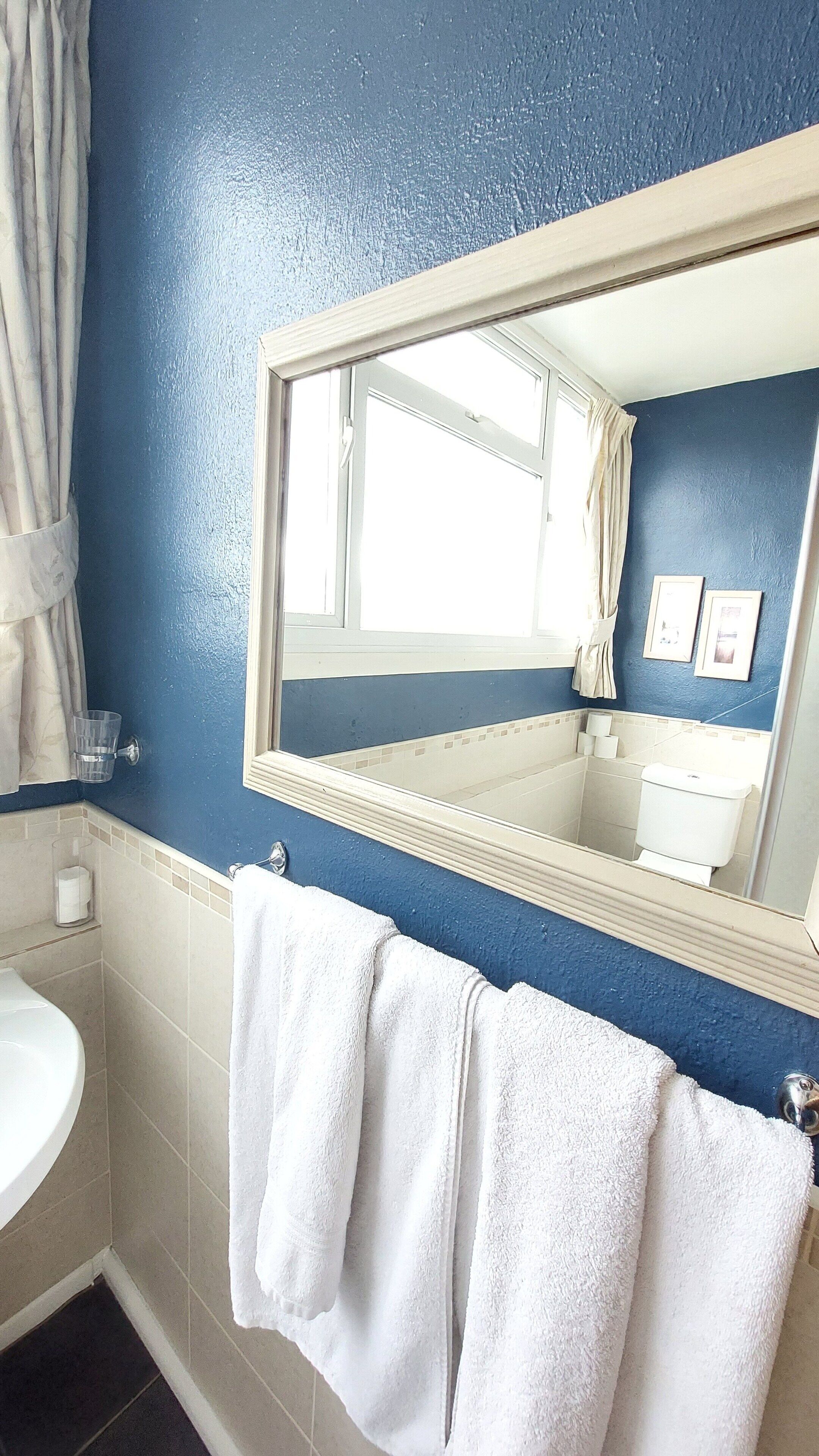A bathroom with a blue wall, a white sink, a mirror, and two white towels hanging on the wall.