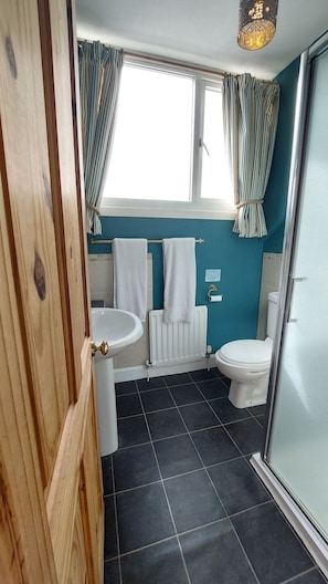 A bathroom with a white sink, toilet, and bathtub. There are two towels hanging on the wall. The floor is tiled, and there is a window with curtains.