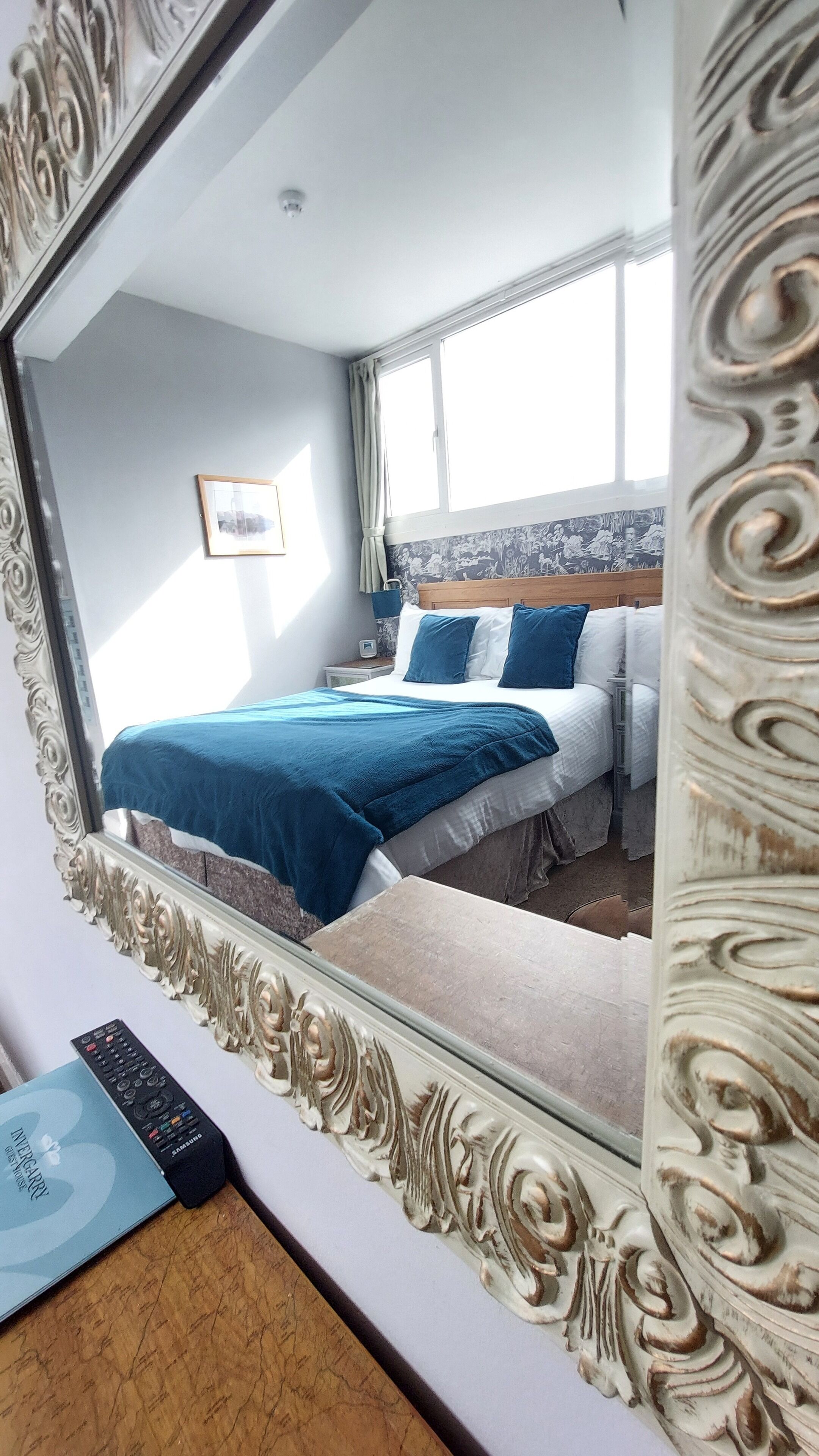 A bedroom with a bed, a bedside table, a mirror, and a window.