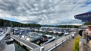 A marina with various boats docked, a wooden pier, and a person standing near a craft beer tent. - Invergarry Room Only Guest House (Windermere)