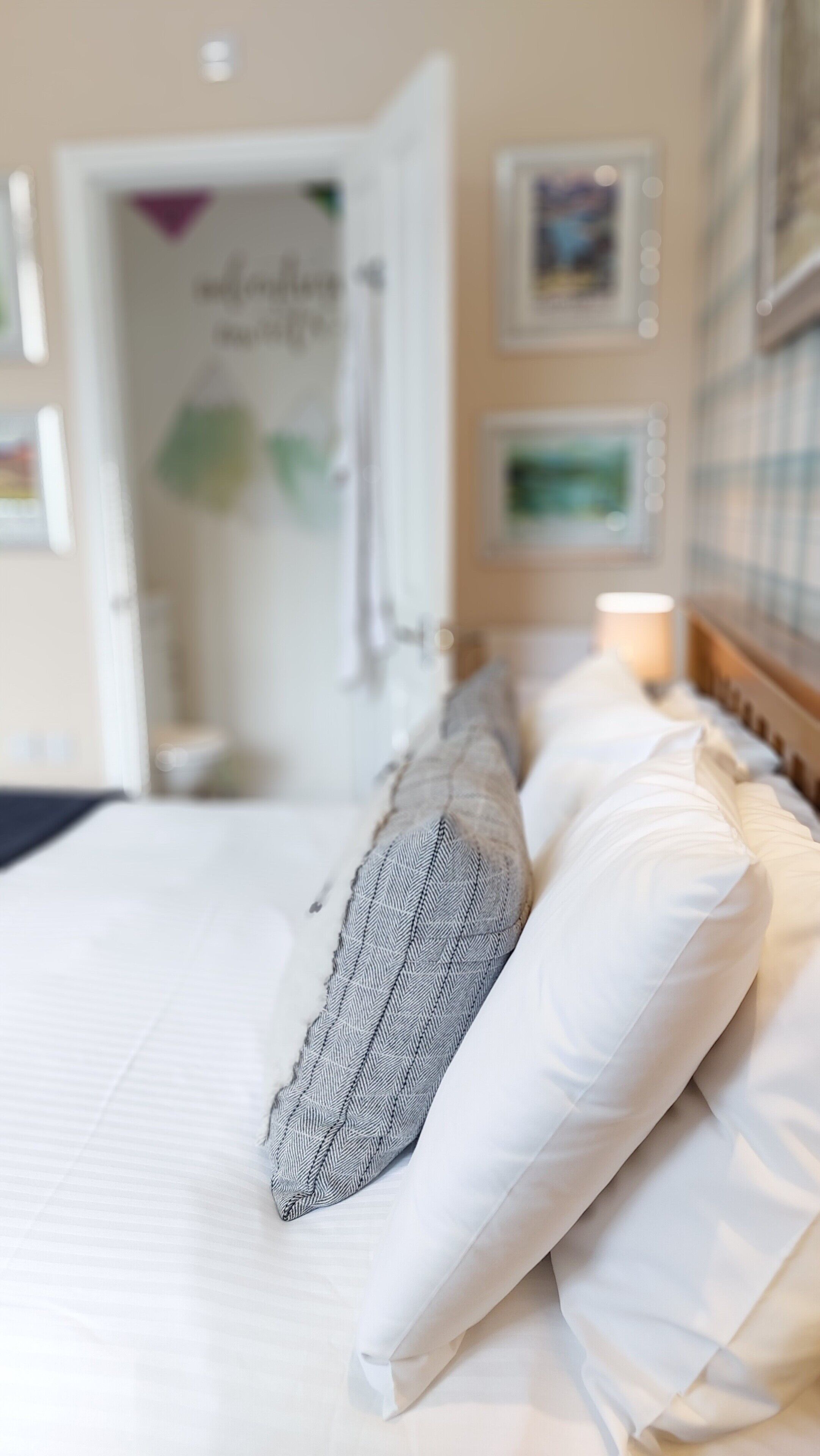 Ein ordentlich bezogenes Bett mit weißen und gemusterten Kissen, einem Holzkopfschild und einer Nachttischlampe.