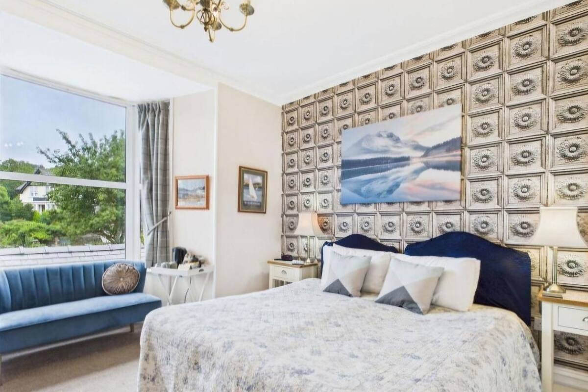 Ein Schlafzimmer mit einem Bett, einem blauen Sofa, einem großen Fenster und einer Wandverzierung.