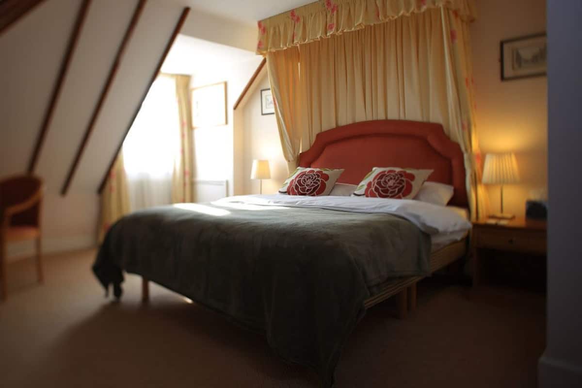 A bedroom with a large bed, a canopy, two bedside lamps, and a chair.