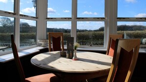 Un espace repas comprenant une table ronde, des chaises et une vue sur un vignoble, visible à travers de grandes fenêtres.
