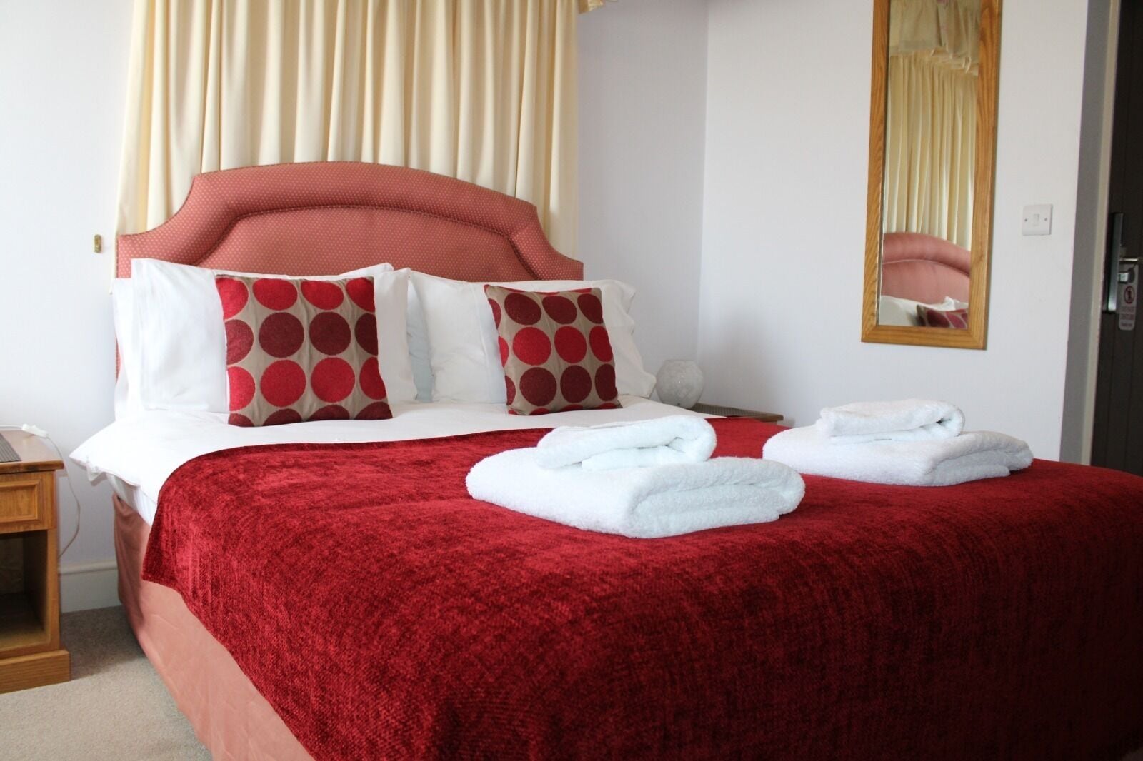 Une chambre d’hôtel avec un lit, des oreillers, une table de chevet, un miroir et des serviettes.