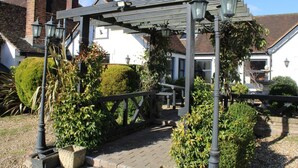 Il s’agit d’un bâtiment traditionnel doté d’un espace extérieur abrité avec des sièges, d’une cheminée en briques et d’un jardin bien entretenu agrémenté de haies et de plantes en pot.