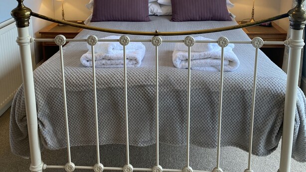 Un lit bien fait, avec un cadre en métal blanc, deux oreillers et une couverture. On y trouve deux lampes de chevet et un tableau encadré accroché au mur.