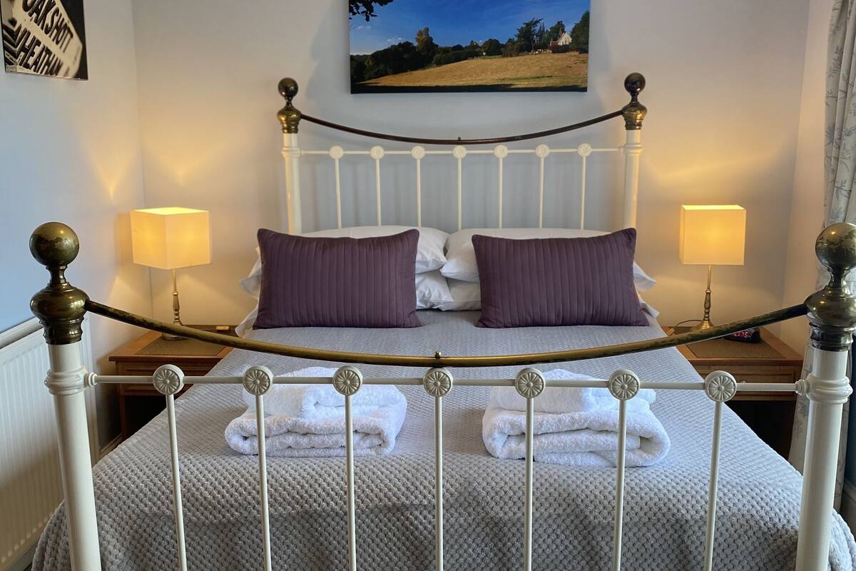 A neatly made bed with a white metal frame, two pillows, and a blanket. There are two bedside lamps and a framed picture on the wall.