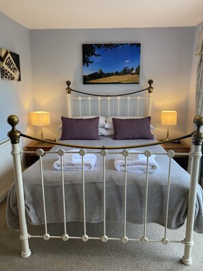 A neatly made bed with a white metal frame, two pillows, and a blanket. There are two bedside lamps and a framed picture on the wall. - The Trooper Inn (Petersfield)