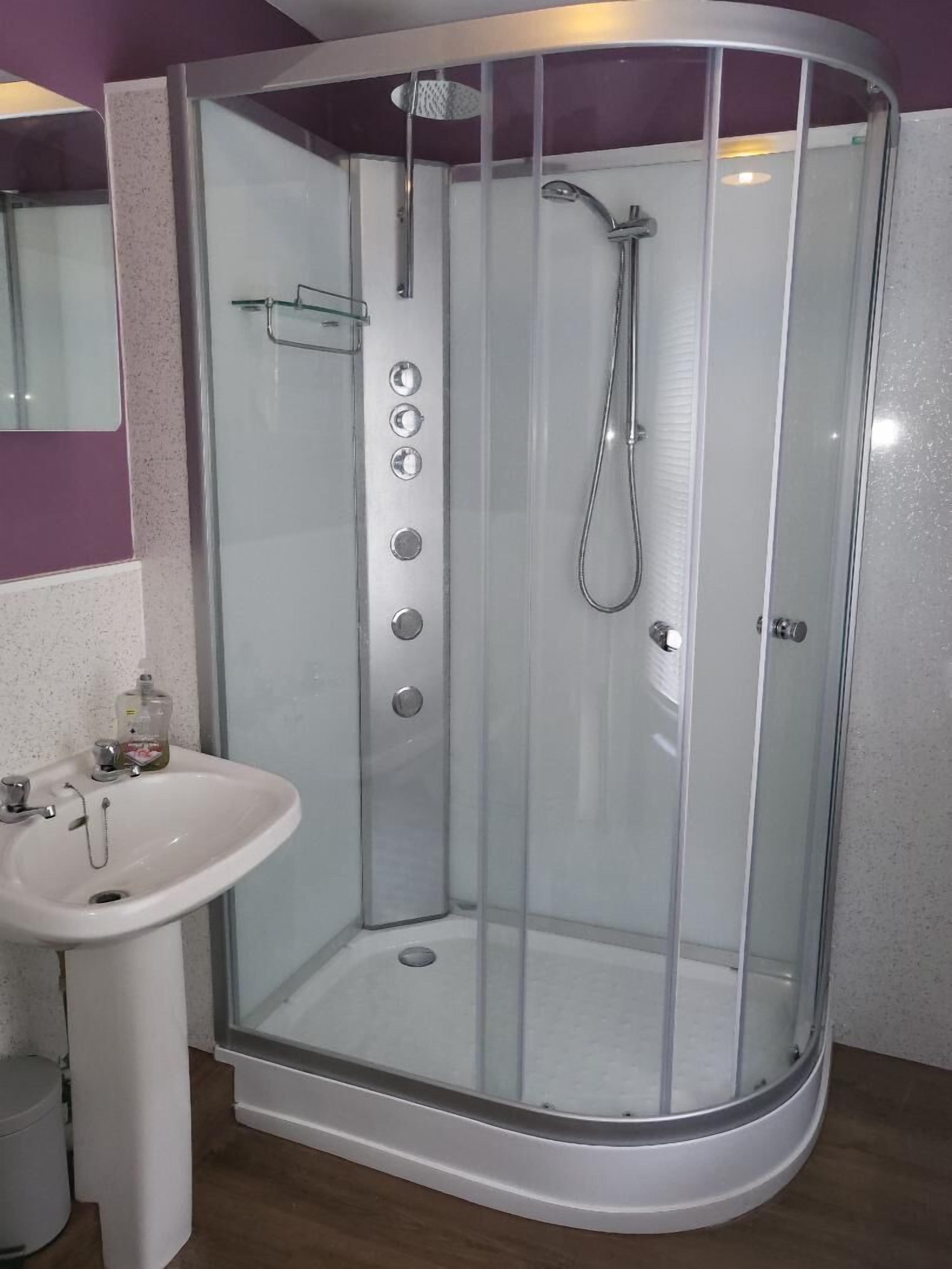 Cabina de ducha con puerta de vidrio, un lavamanos y un espejo.