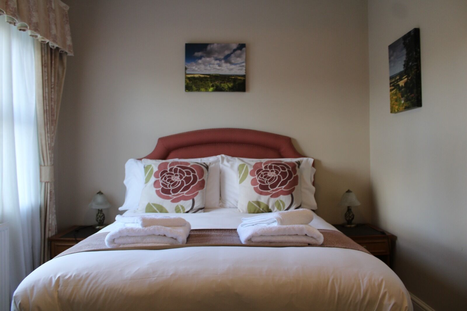 A neatly made bed with two pillows, a headboard, and two bedside tables with lamps.
