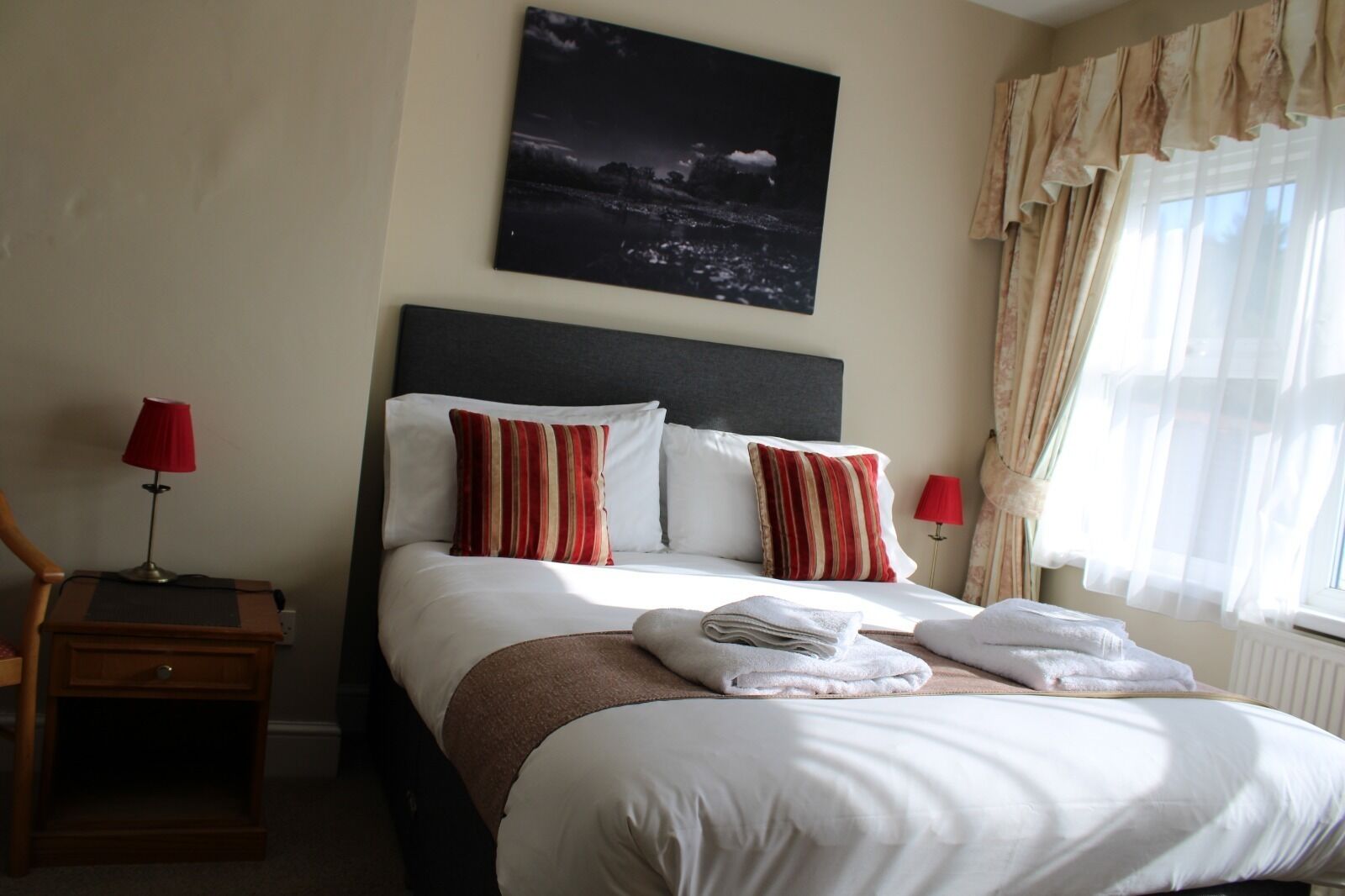 A hotel room with a bed, two bedside lamps, a night sky painting, and a window with curtains.