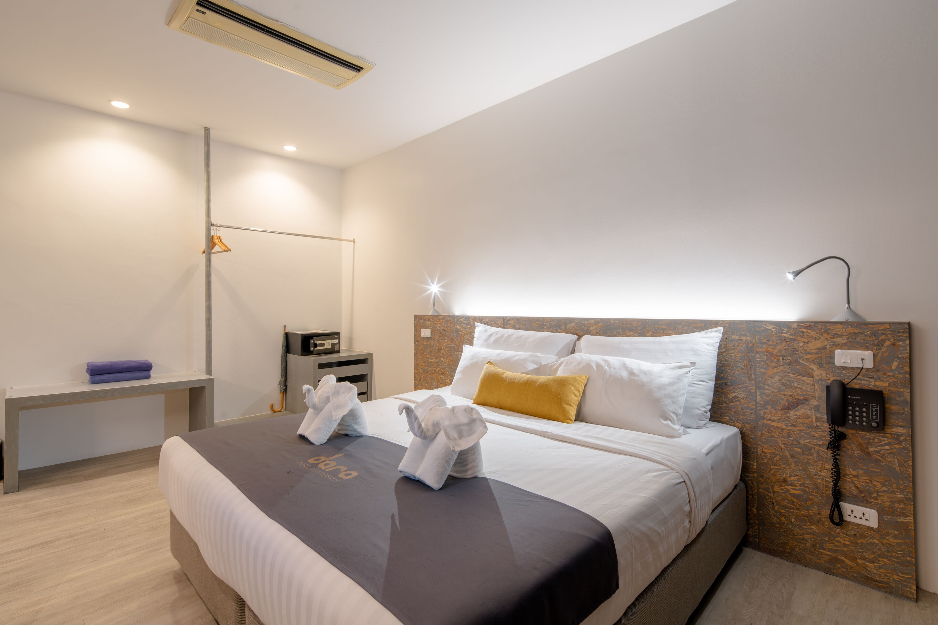 Una habitación de hotel moderna con una cama bien hecha, una mesita de noche con lámpara, teléfono y aire acondicionado instalado en la pared.