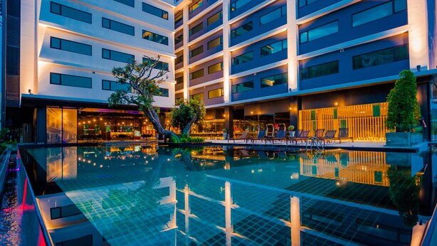 Un hôtel moderne doté d’une grande piscine intérieure, de plusieurs étages et d’une façade bien éclairée.