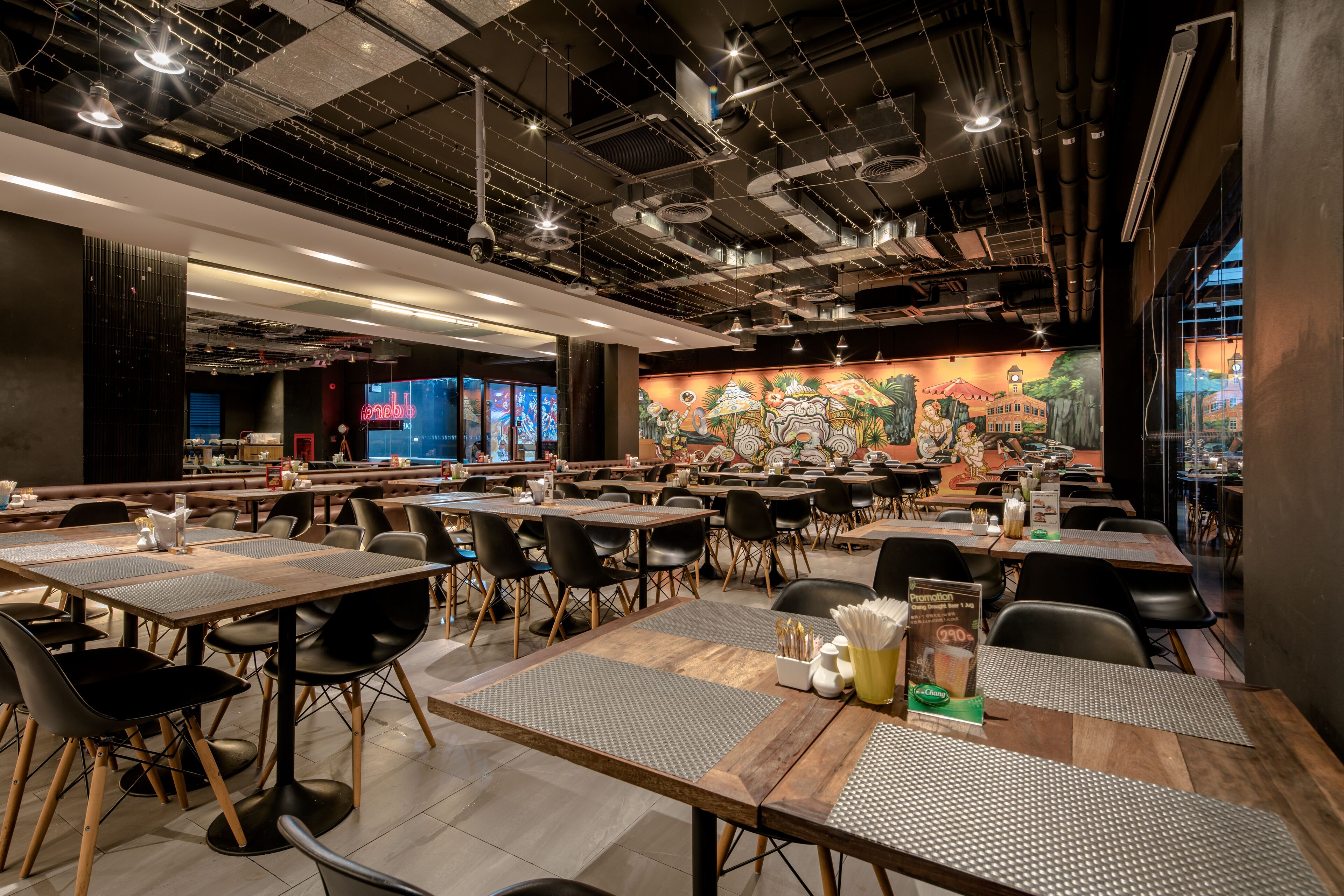 Un restaurante espacioso con varias mesas y sillas, un mural en la pared y un diseño de techo moderno.