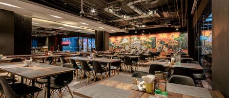 Un restaurante espacioso con varias mesas y sillas, un mural en la pared y un diseño de techo moderno.