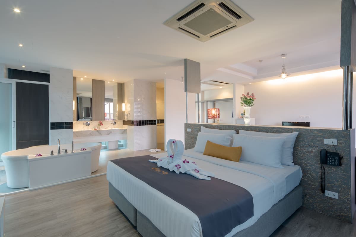 Una habitación de hotel moderna con una cama grande, un baño separado con bañera, un tocador con espejo y un teléfono en la pared.