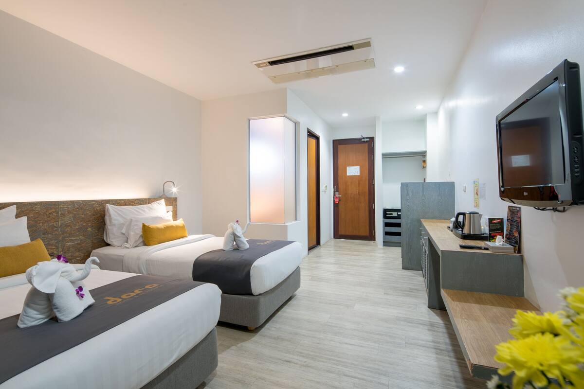 Habitación de hotel con dos camas, un escritorio, televisión y kitchenette.