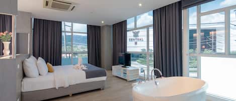 A modern hotel room with a large bed, a TV, a bathtub, and a view of a building with 'CENTRAL' written on it.