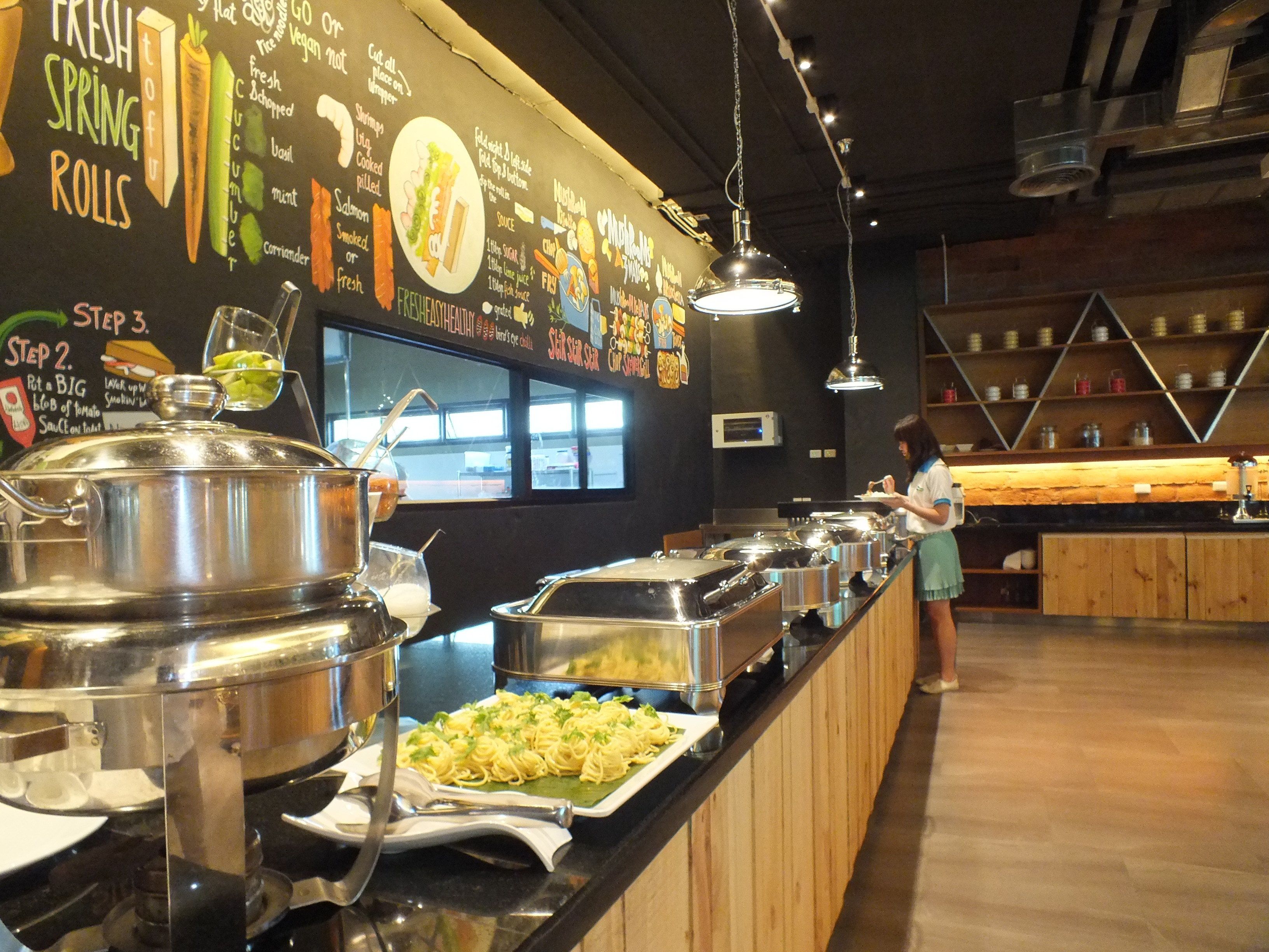 Un espace buffet avec différents stands de nourriture et une personne qui sert les plats.