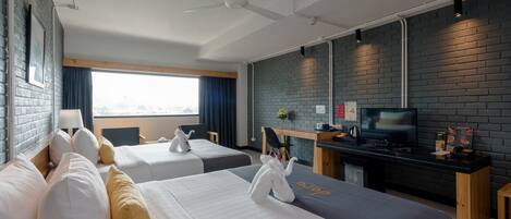A hotel room with two beds, a desk with a TV, and a brick wall.