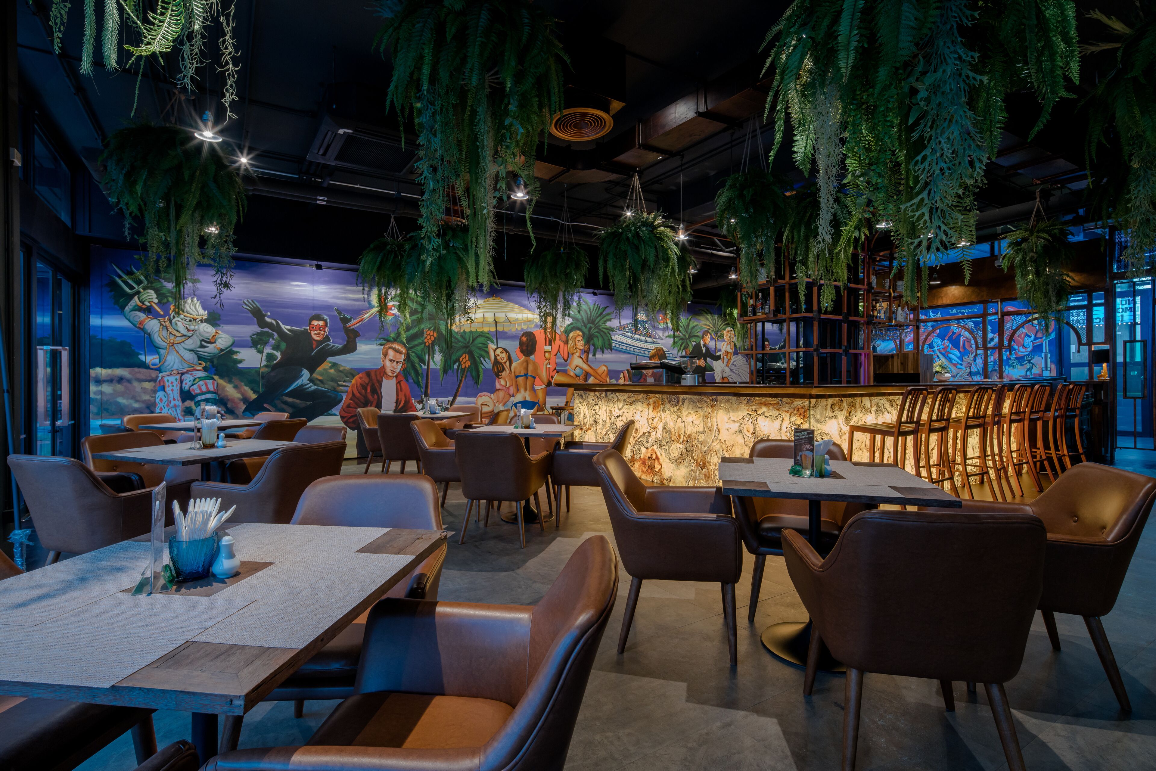 A restaurant interior with hanging plants, a mural, and a bar area.
