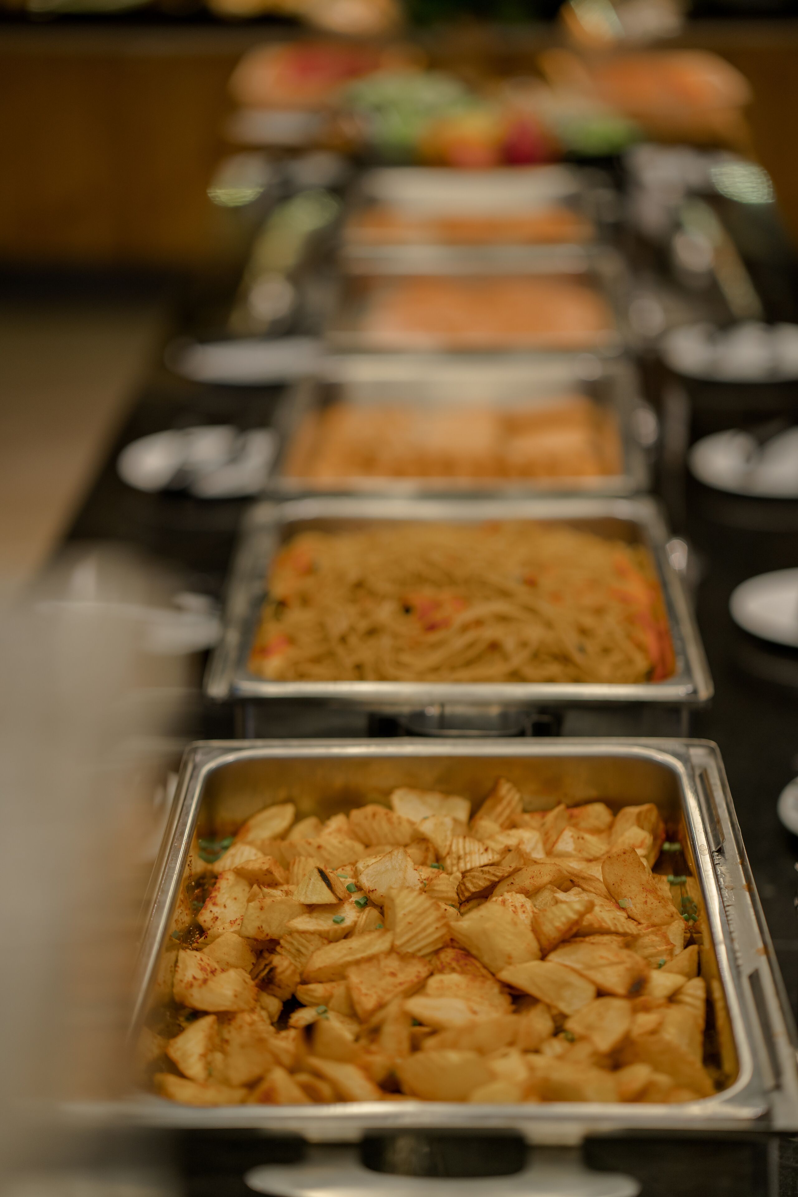 Una barra de buffet con diversas opciones de comida, incluyendo pasta, arroz y un plato con cubos de patata.