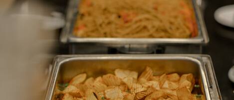 Una barra de buffet con diversas opciones de comida, incluyendo pasta, arroz y un plato con cubos de patata.