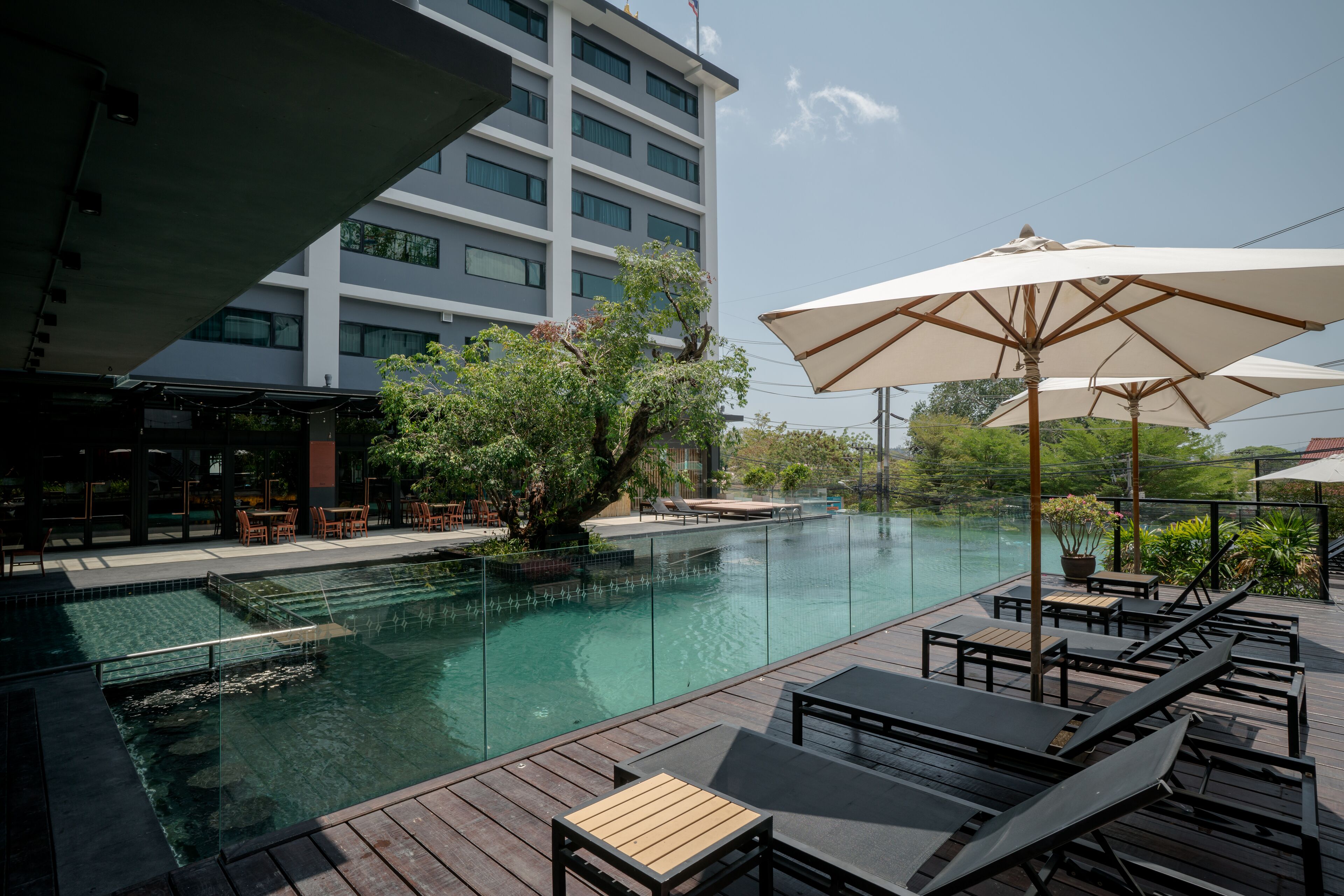 A poolside area with lounge chairs and umbrellas, a clear pool, and a modern building in the background.
