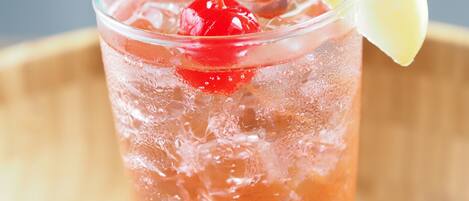 Un vaso de bebida roja con una cereza y una rodaja de limón, rodeado de cubitos de hielo.