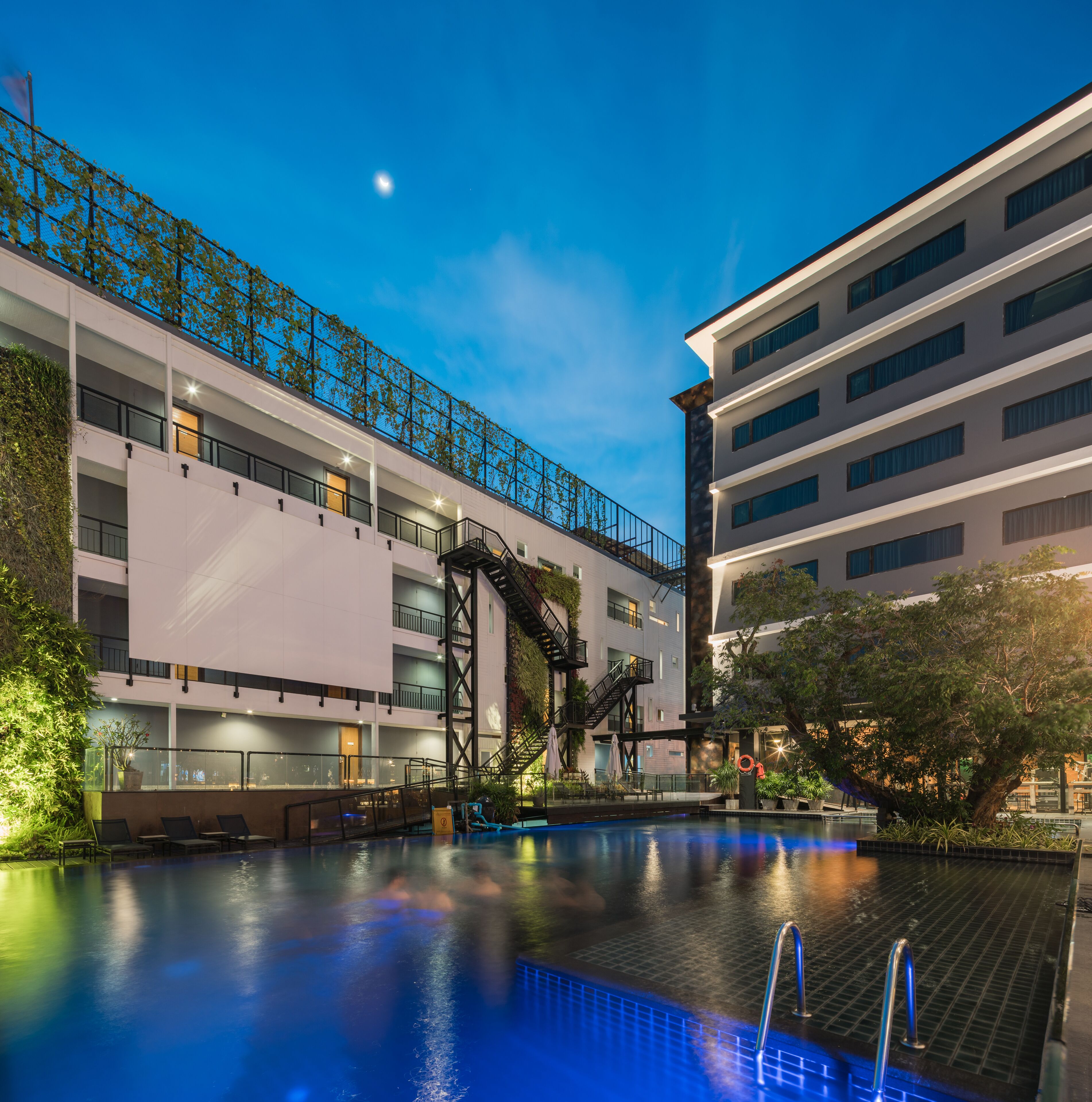 A modern building with a pool, outdoor seating, and a staircase leading to a balcony.