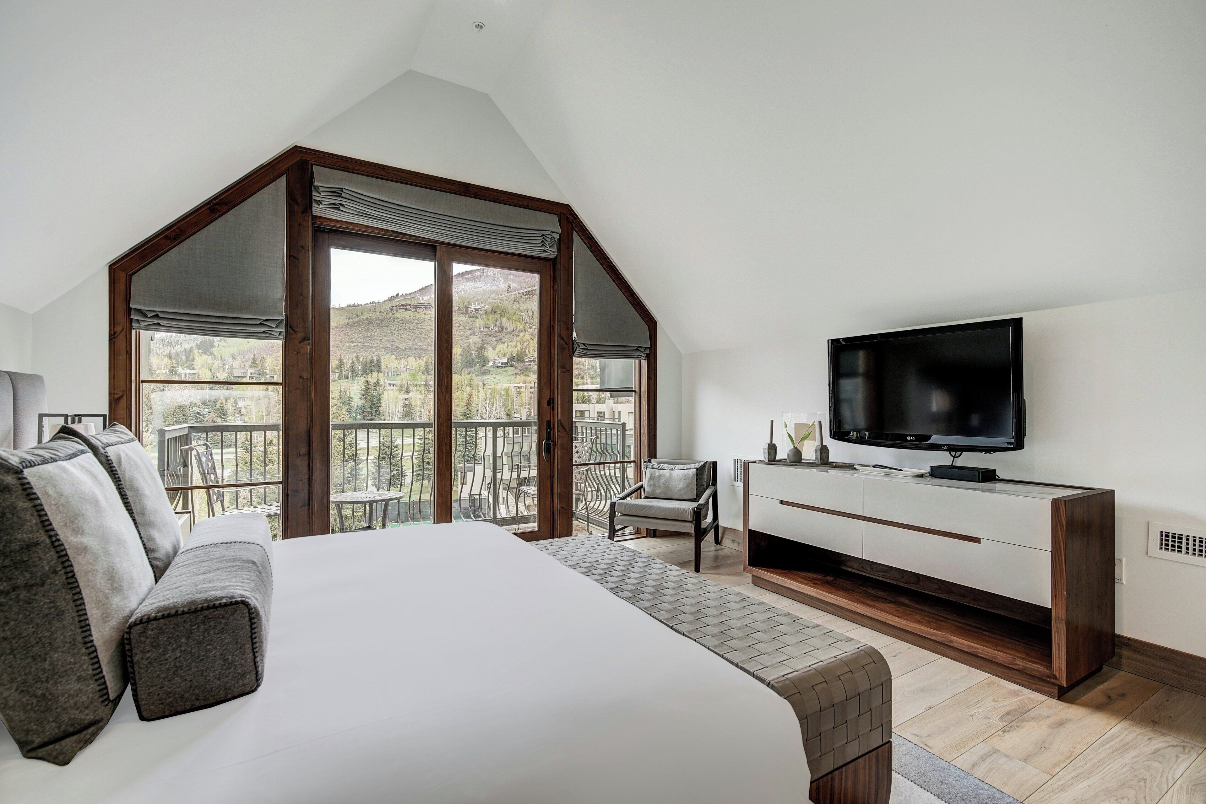 A bedroom with a large bed, a TV, a chair, and a balcony with a view of the outdoors.