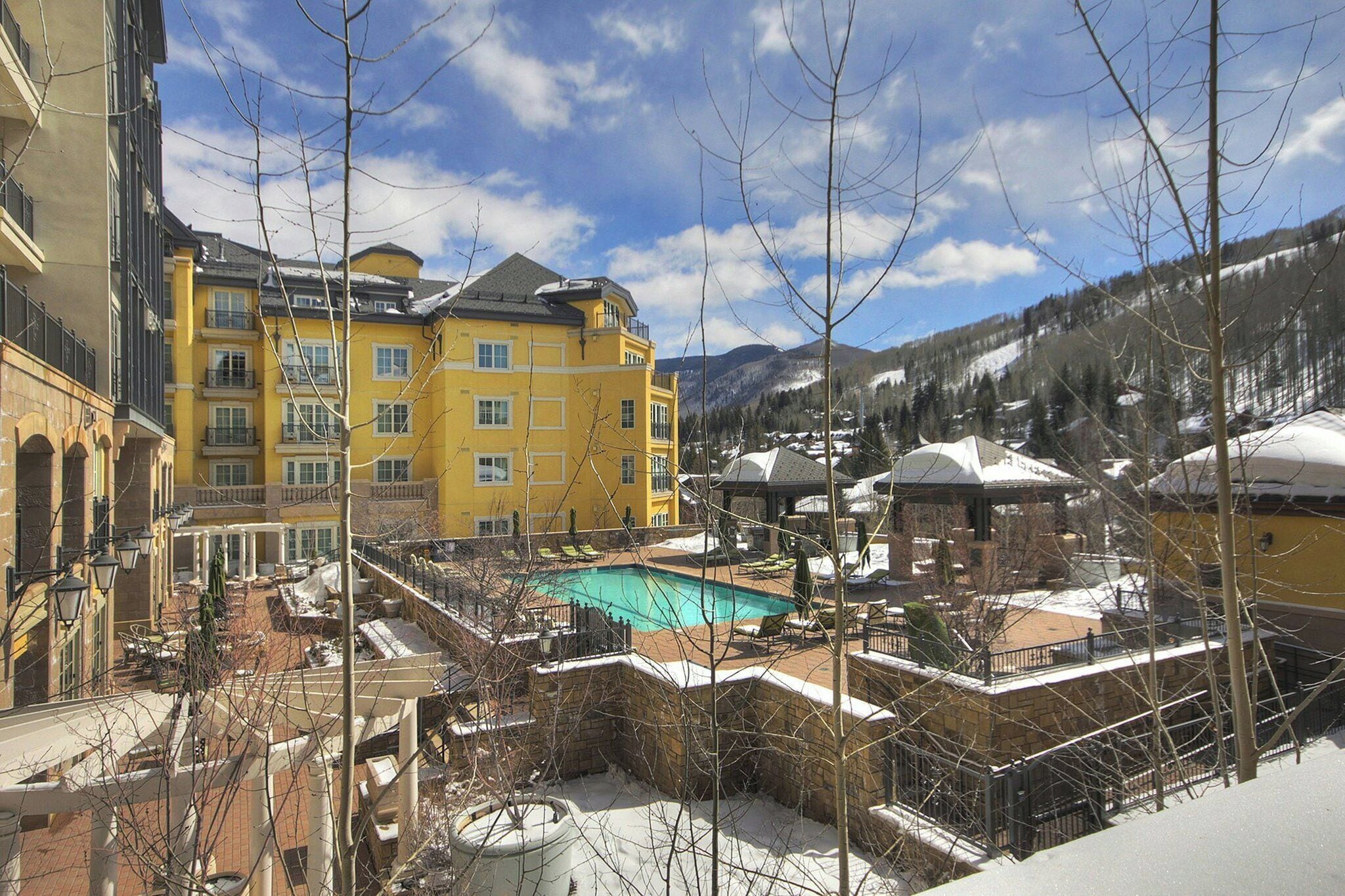 A hotel with a pool, snow-covered surroundings, and mountains in the background.
