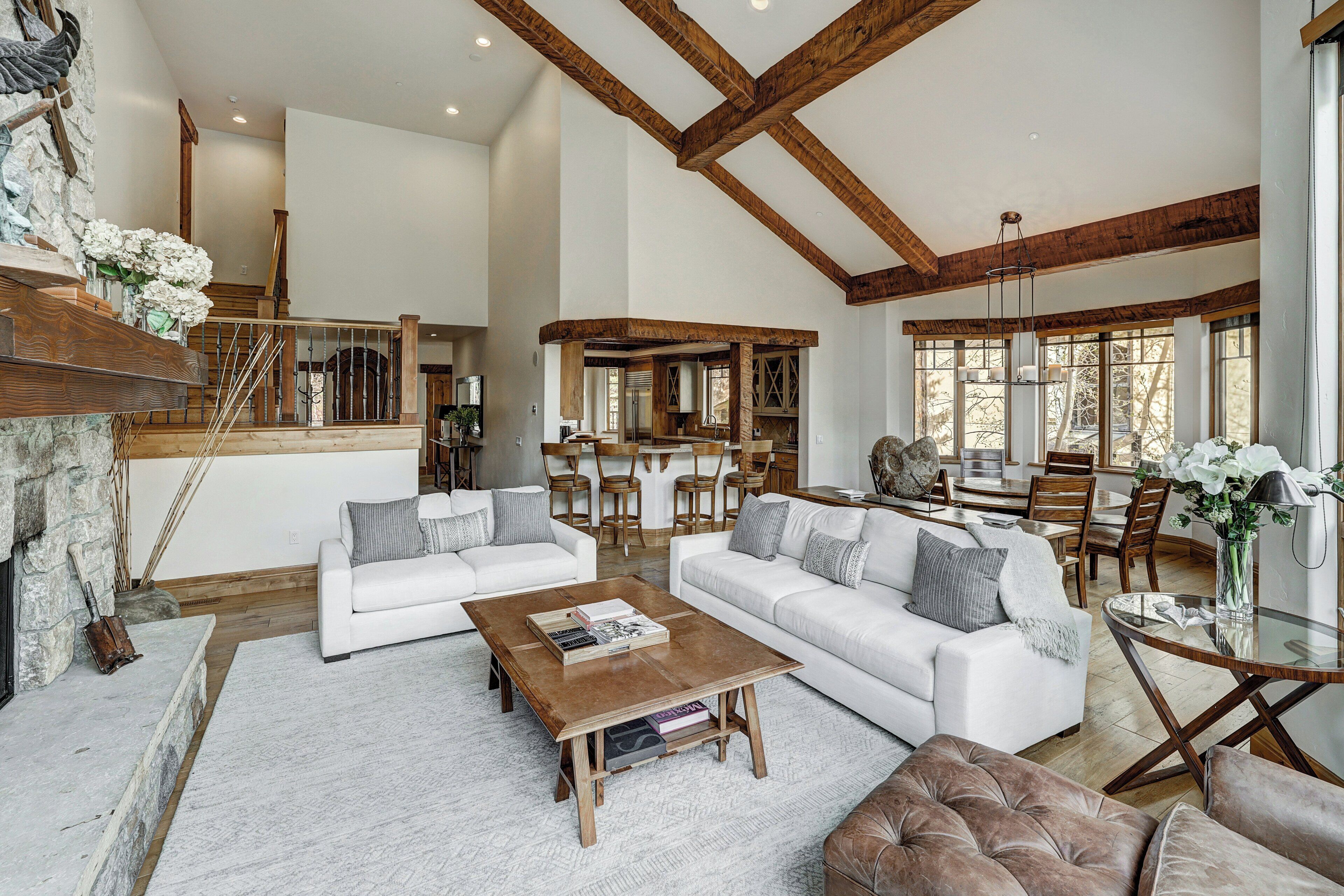 A spacious living room with a fireplace, white sofas, a coffee table, and a dining area with wooden furniture.