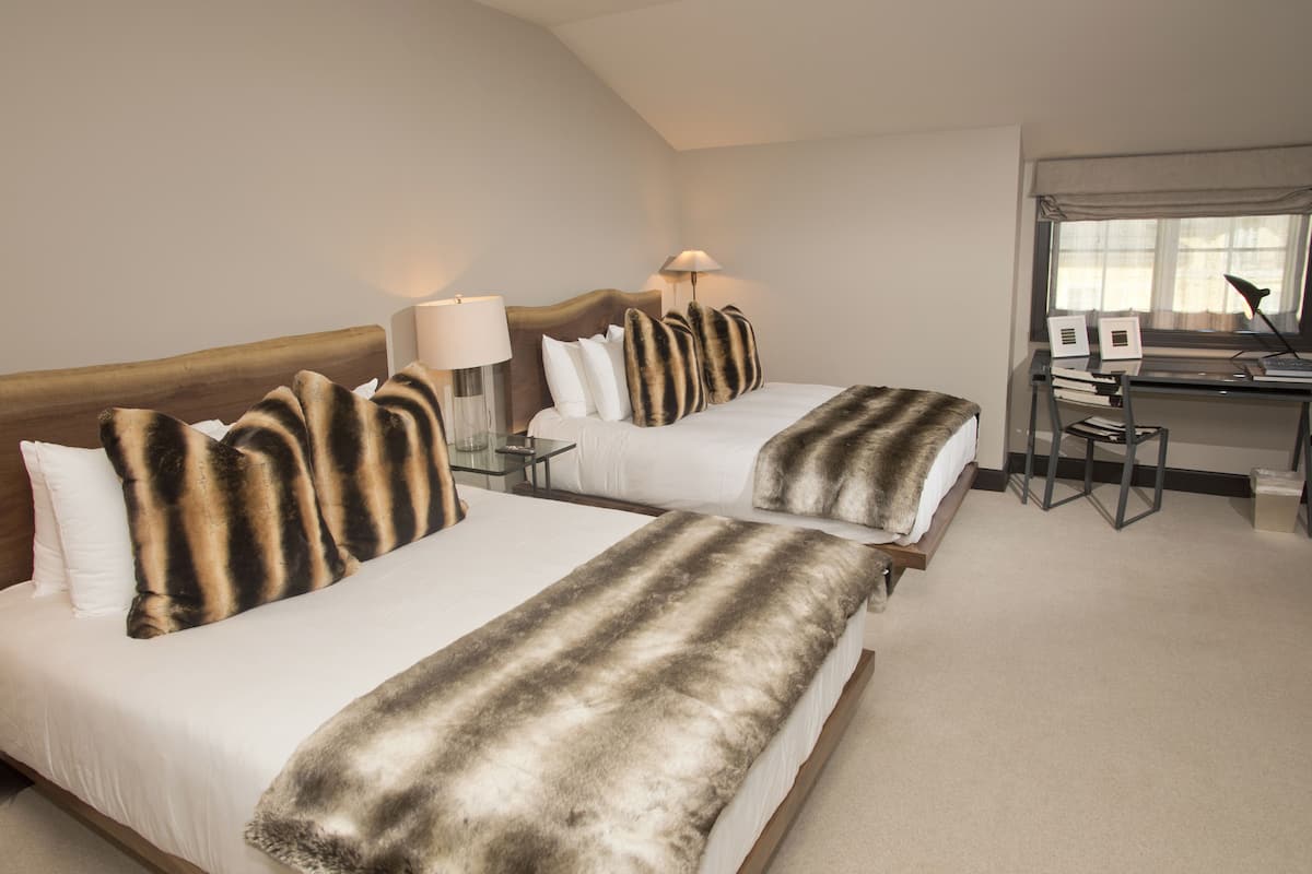 A hotel room with two beds, each with a striped blanket, a desk with a chair, and a lamp.