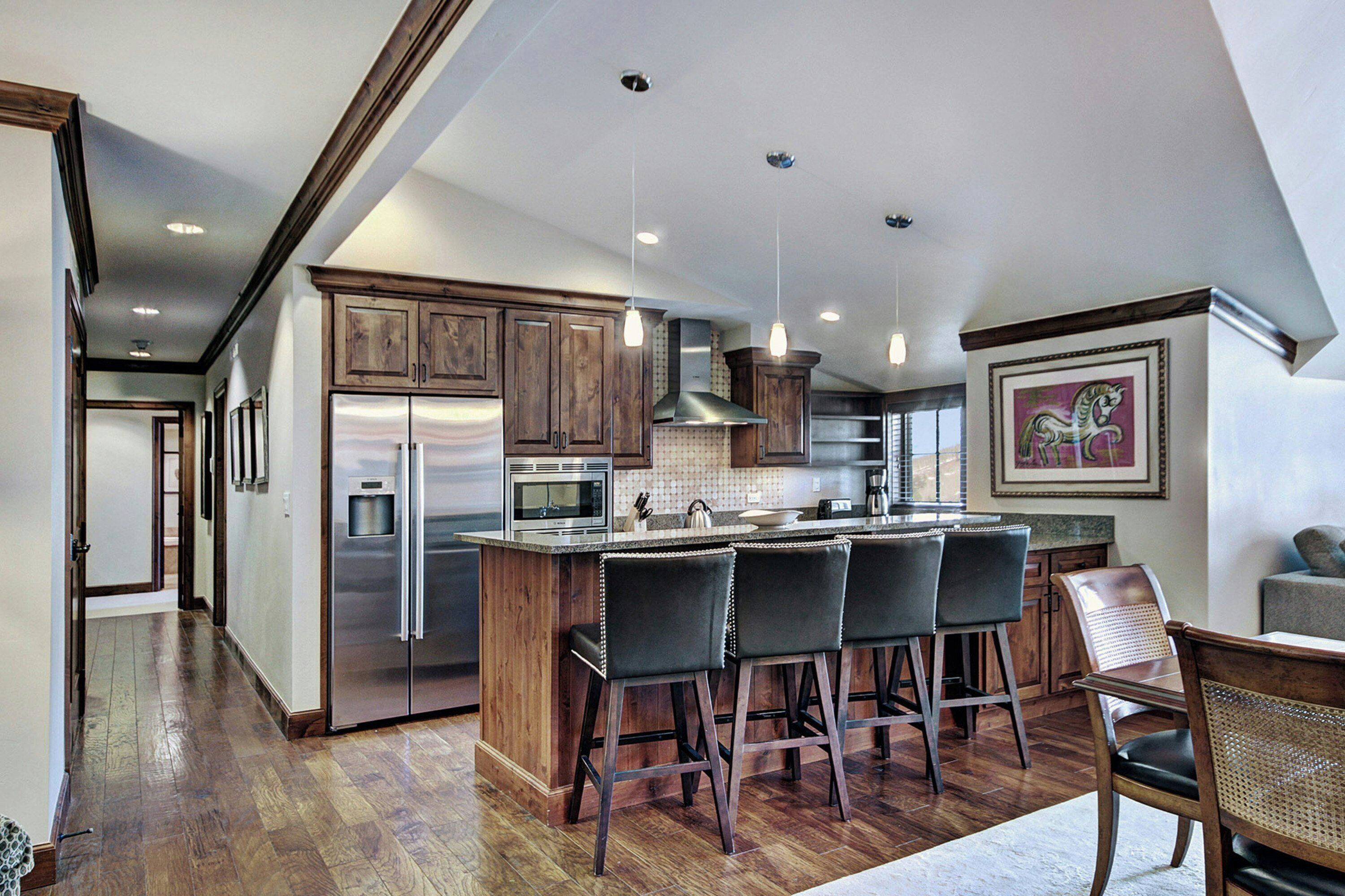 A modern kitchen with a central island, bar stools, stainless steel appliances, and wooden cabinetry.