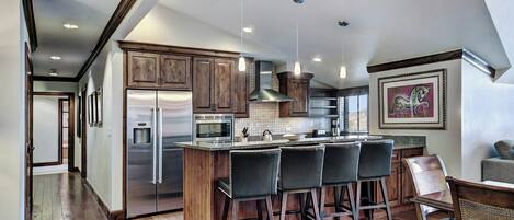 A modern kitchen with a central island, bar stools, stainless steel appliances, and wooden cabinetry.