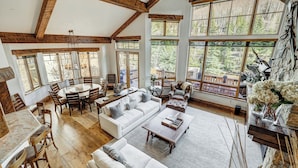 A spacious living area with a high ceiling, wooden beams, large windows, and a view of the outdoors. - Legendary Lodging at the Ritz Carlton Residences Vail (Vail)